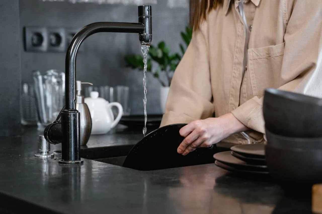 Person washing dishes in modern kitchen with black sink and running water