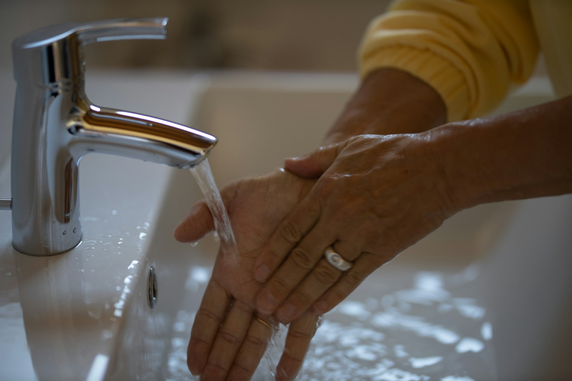 Hands being washed with water flowing from a modern chrome faucet