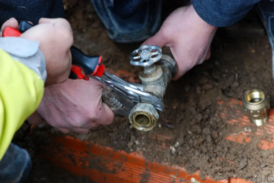 Hands using pliers to adjust valve on muddy industrial equipment