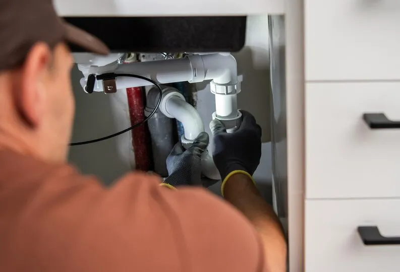 Plumber fixing pipes under sink with gloved hands