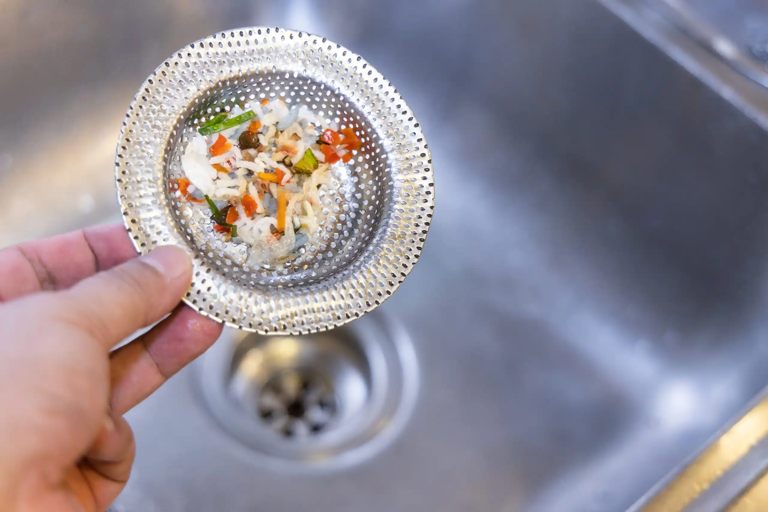 Perforated metal strainer with chopped vegetables over kitchen sink