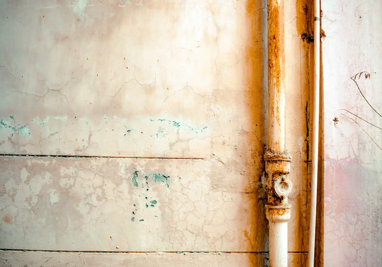 Rusty water pipes on weathered wall with faded green and orange tones