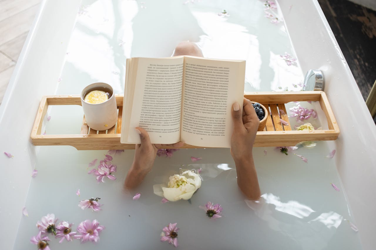 Relaxing bath with open book, tea, and scattered pink flowers
