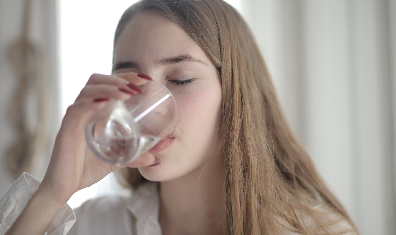 Young woman drinking water with eyes closed in soft-lit room
