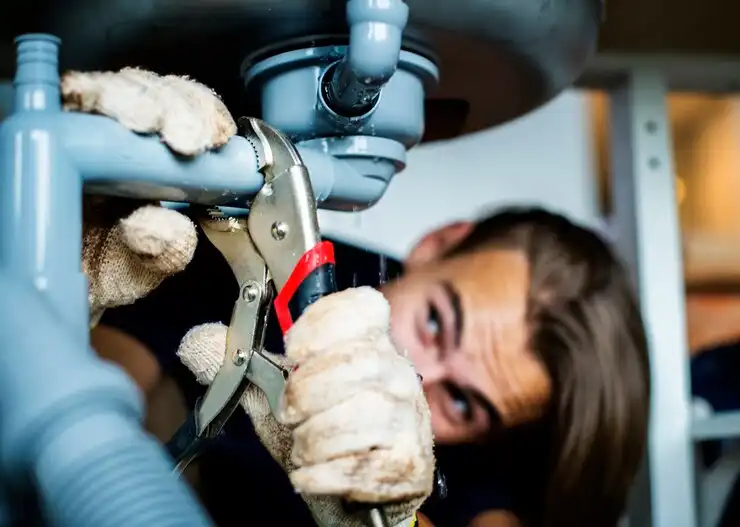 Plumber fixing pipes using pliers under sink with focused expression
