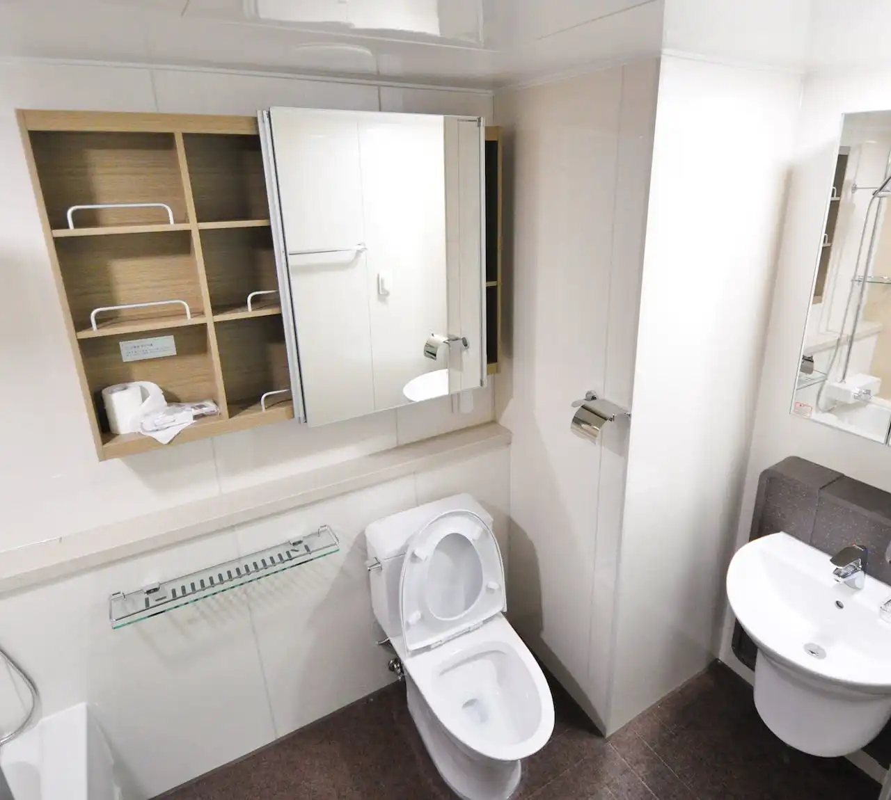 Clean, modern bathroom with white toilet, sink, and wooden shelving unit