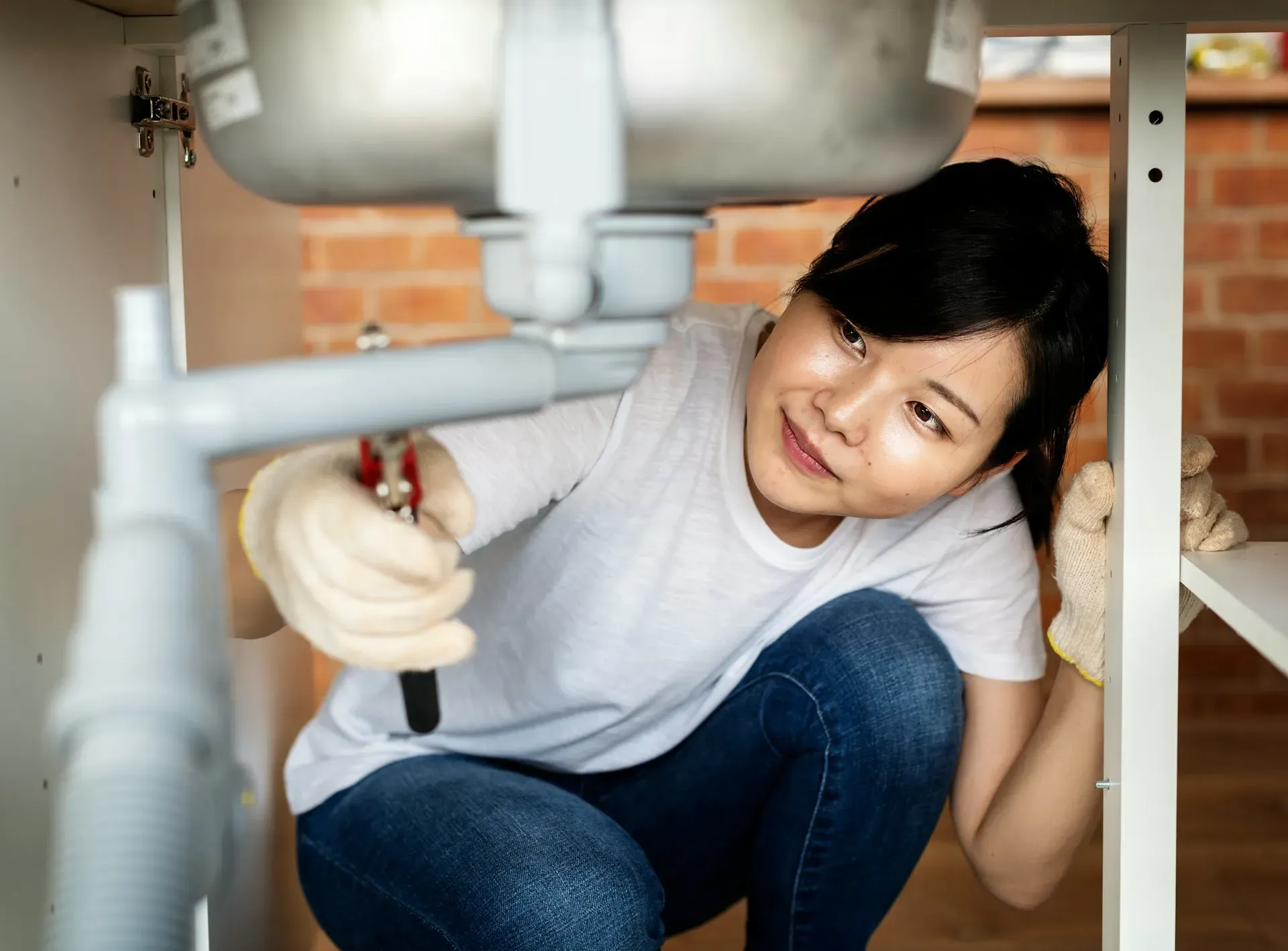Woman fixing sink pipes under cabinet with wrench