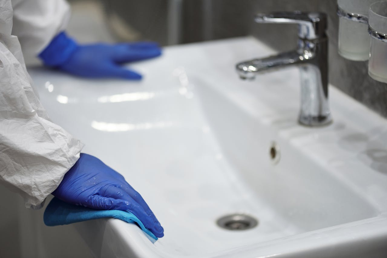 Blue gloved hand cleaning white sink with disinfecting cloth