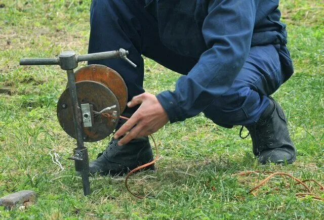 Person operating manual hand-crank grinding wheel on grassy ground