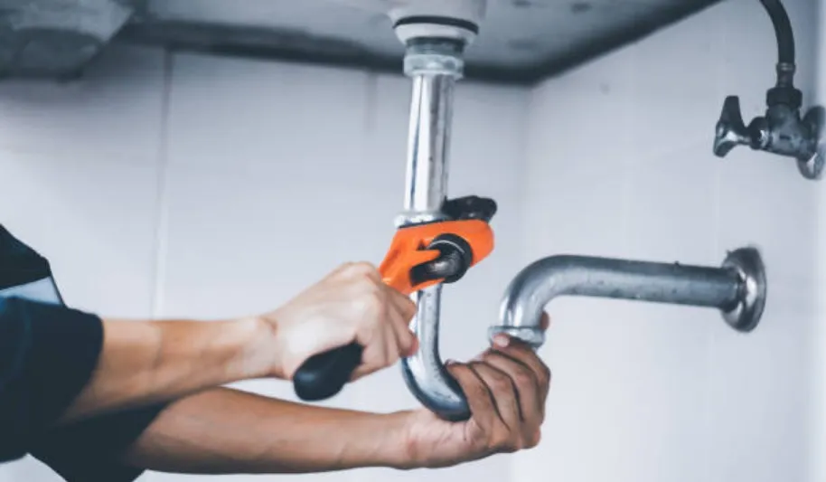 Plumber using orange wrench to repair metal pipe under sink