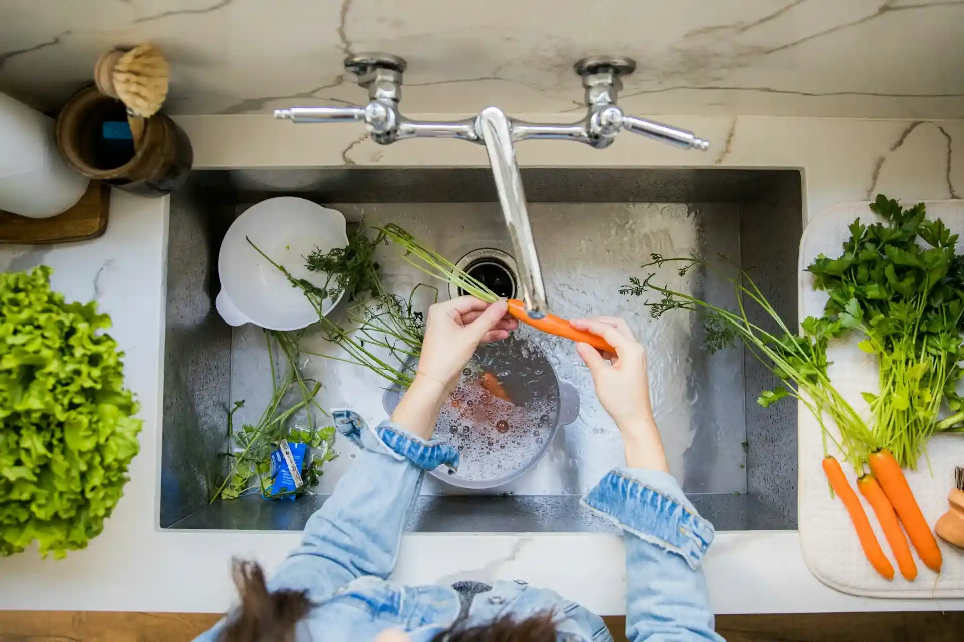 Hands washing fresh carrot under running water in kitchen sink