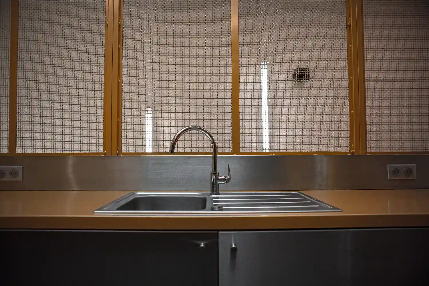 Stainless steel kitchen sink with modern faucet under mesh-covered window