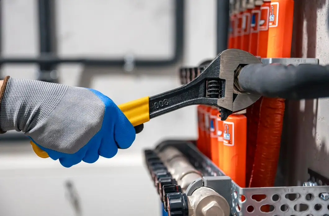 Hand in safety glove using adjustable wrench on industrial pipes