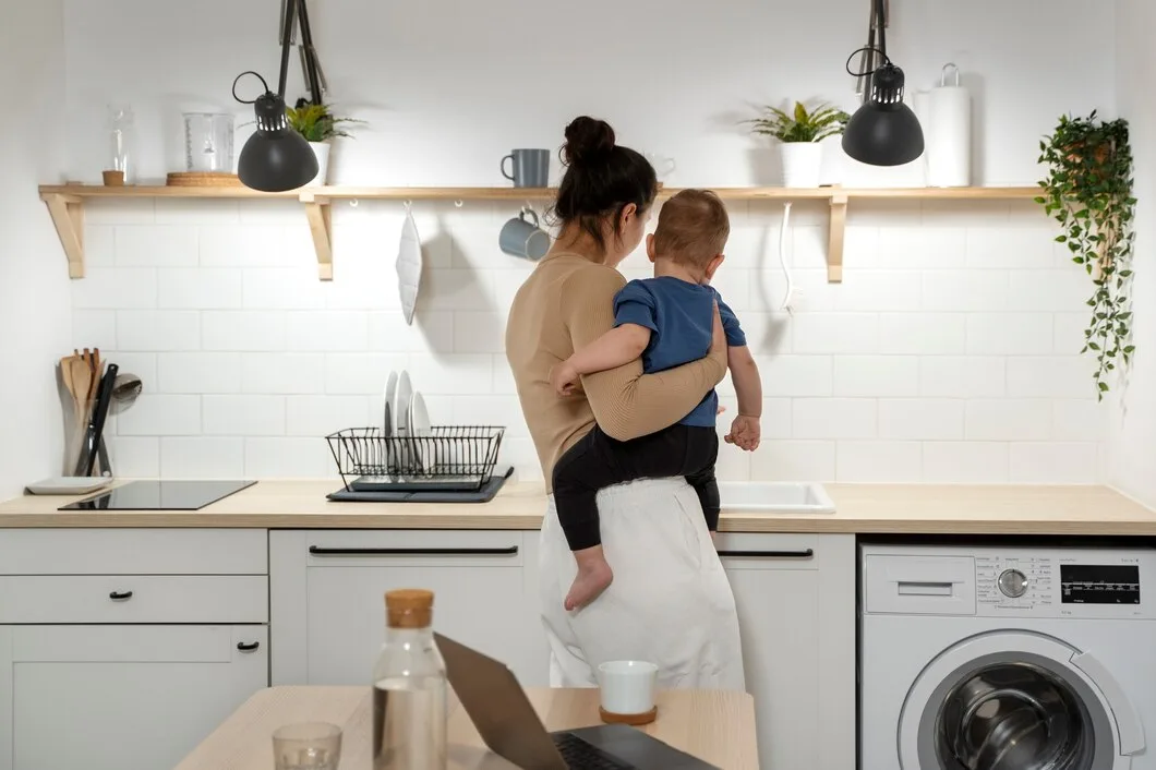 Parent holding child while working in minimalist kitchen with appliances