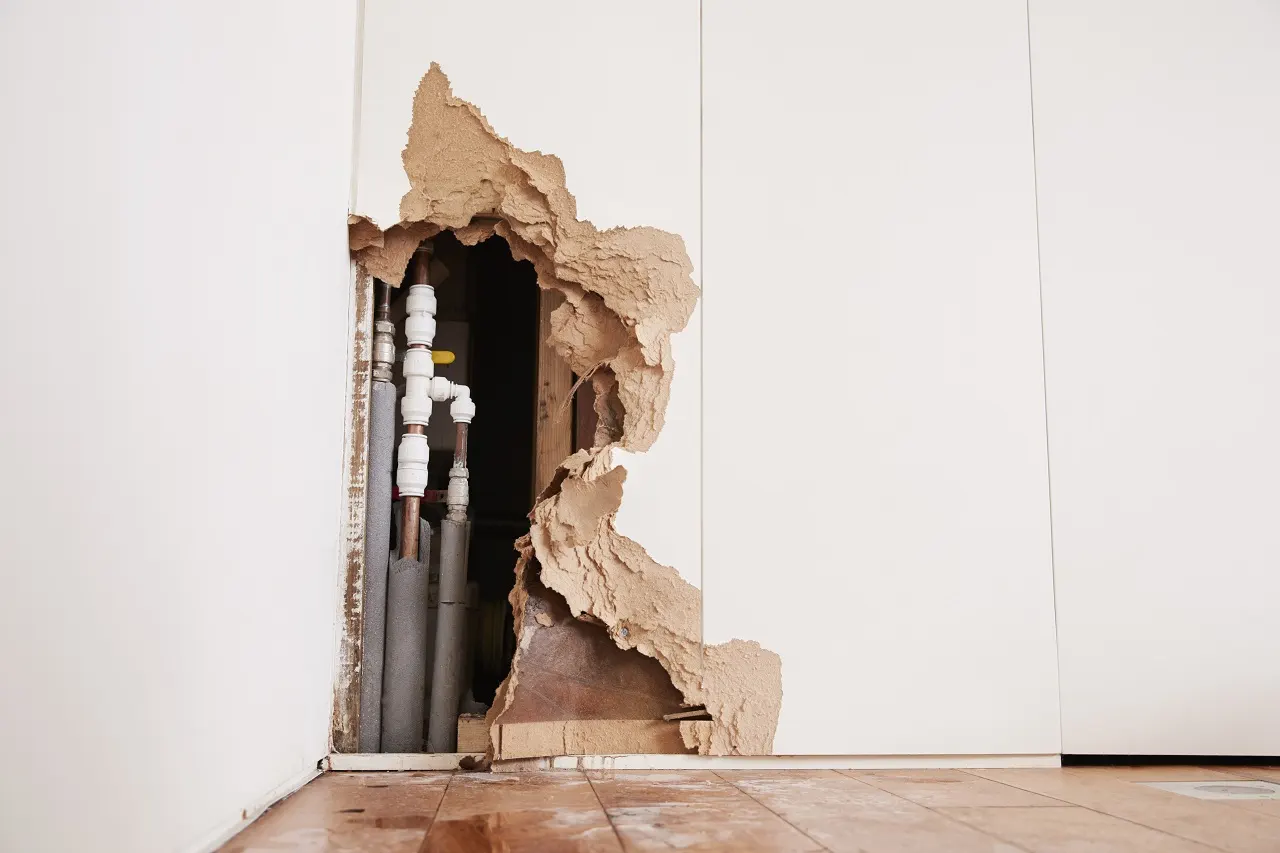 Damaged wall with exposed pipes and crumbling plaster