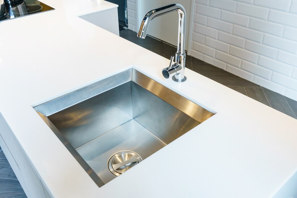 Modern stainless steel kitchen sink with high-arc faucet on white countertop