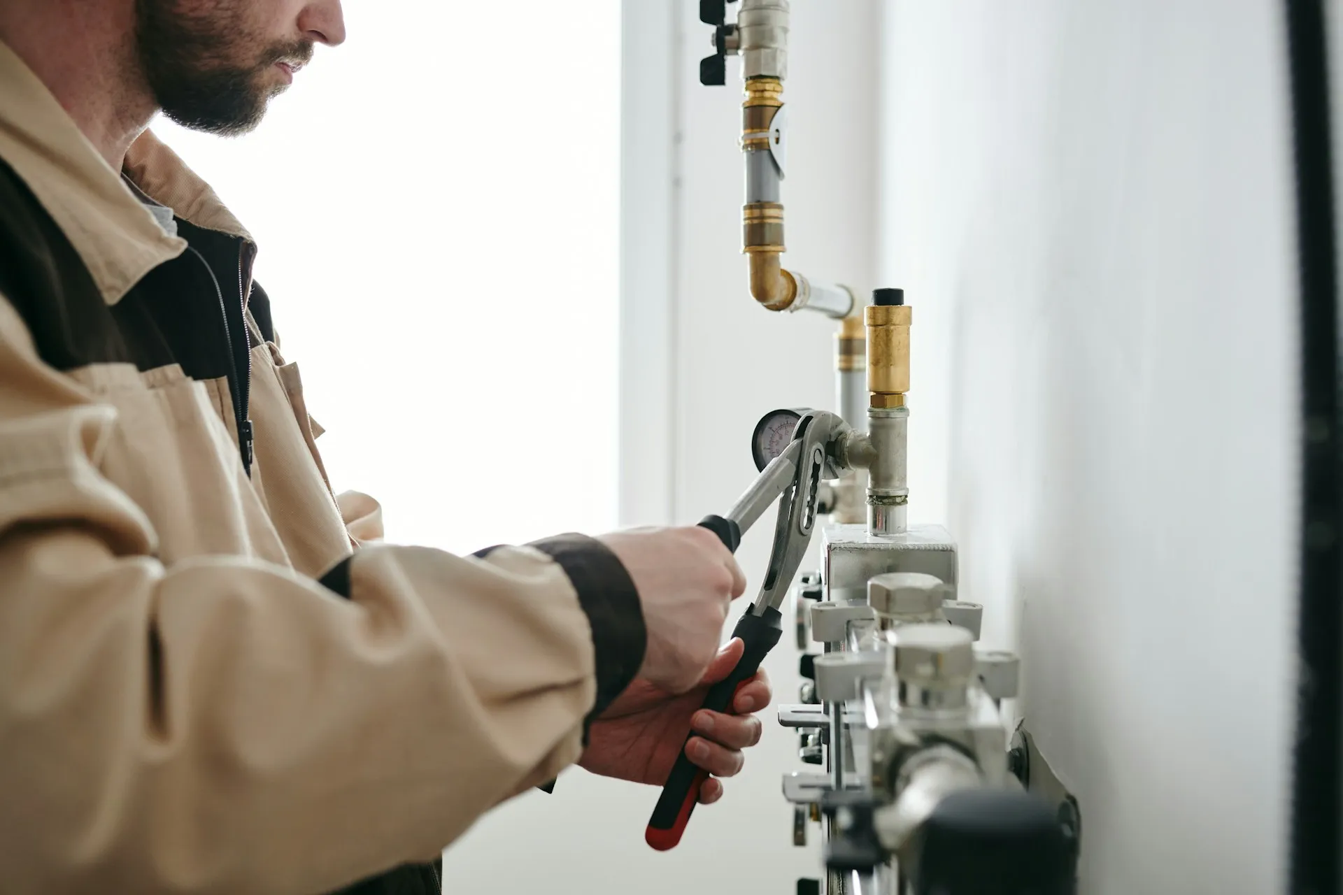 Plumber in beige jacket using wrench to adjust industrial pipe system
