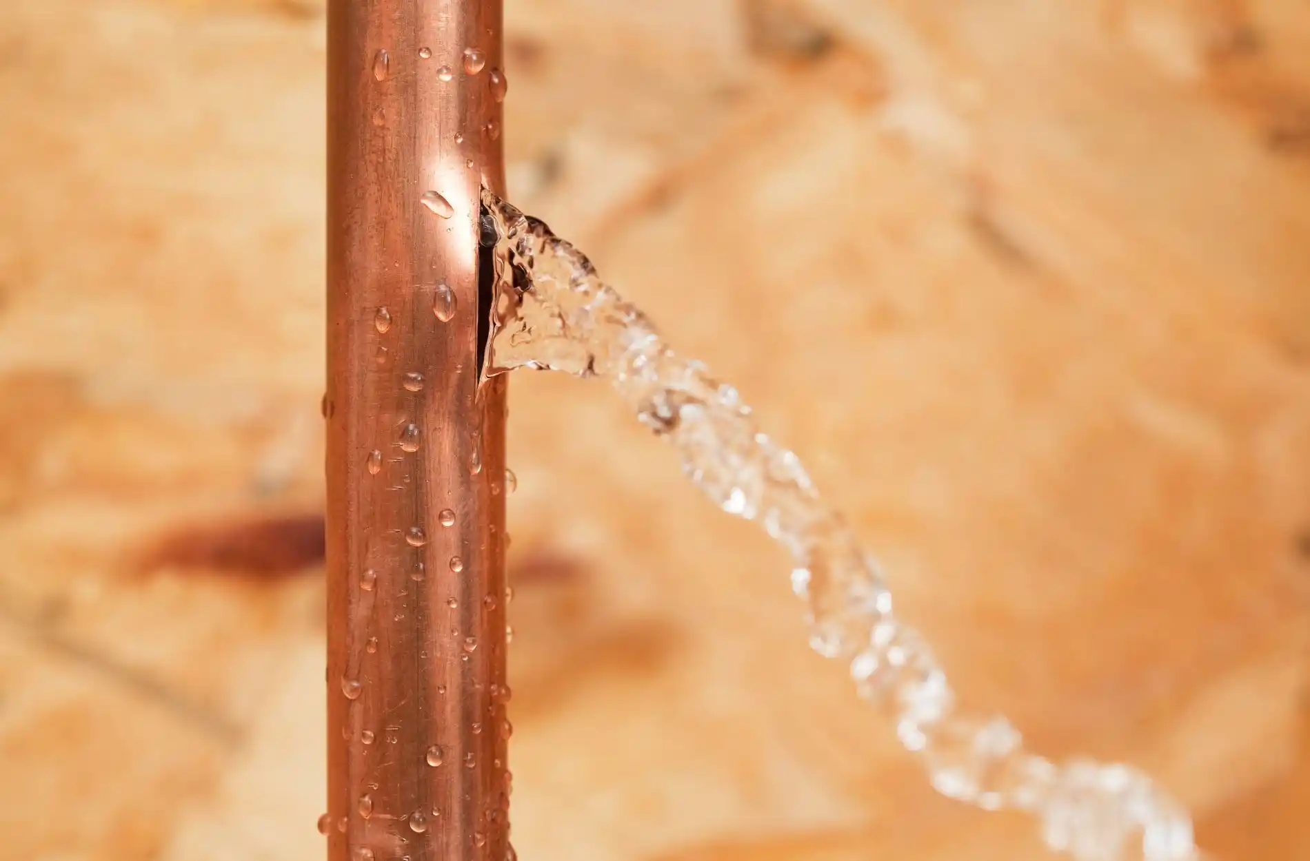 Copper pipe with water droplets and leak spraying water