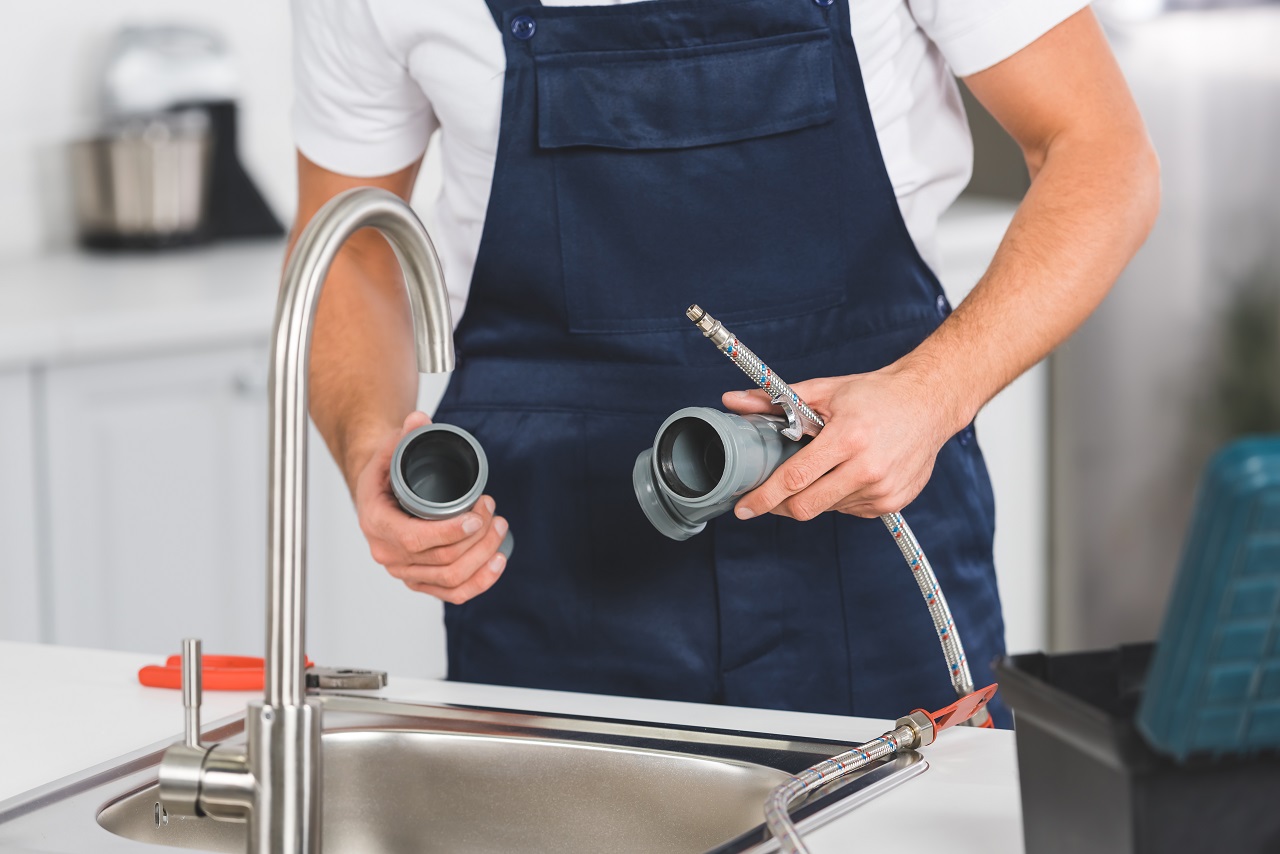 Plumber in blue apron working on sink pipes and connections