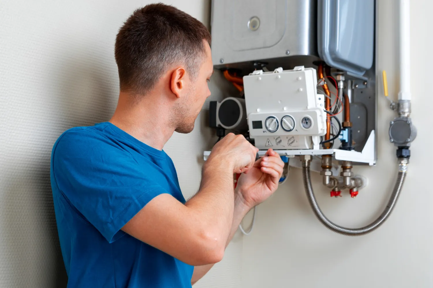 Technician in blue shirt repairing a wall-mounted water heater