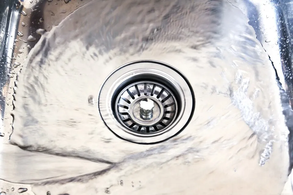 Stainless steel kitchen sink drain with water droplets and blurred background