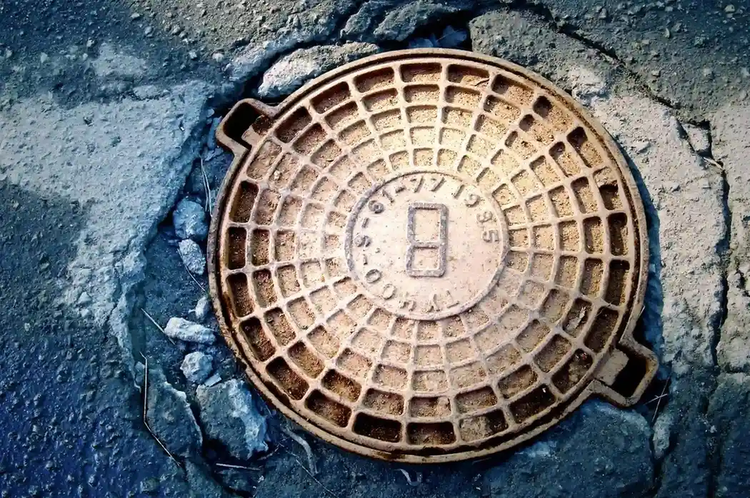 Rusty manhole cover with grid pattern embedded in cracked asphalt street