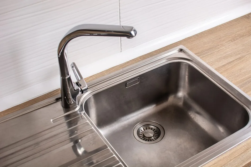 Stainless steel kitchen sink with modern faucet on wooden countertop