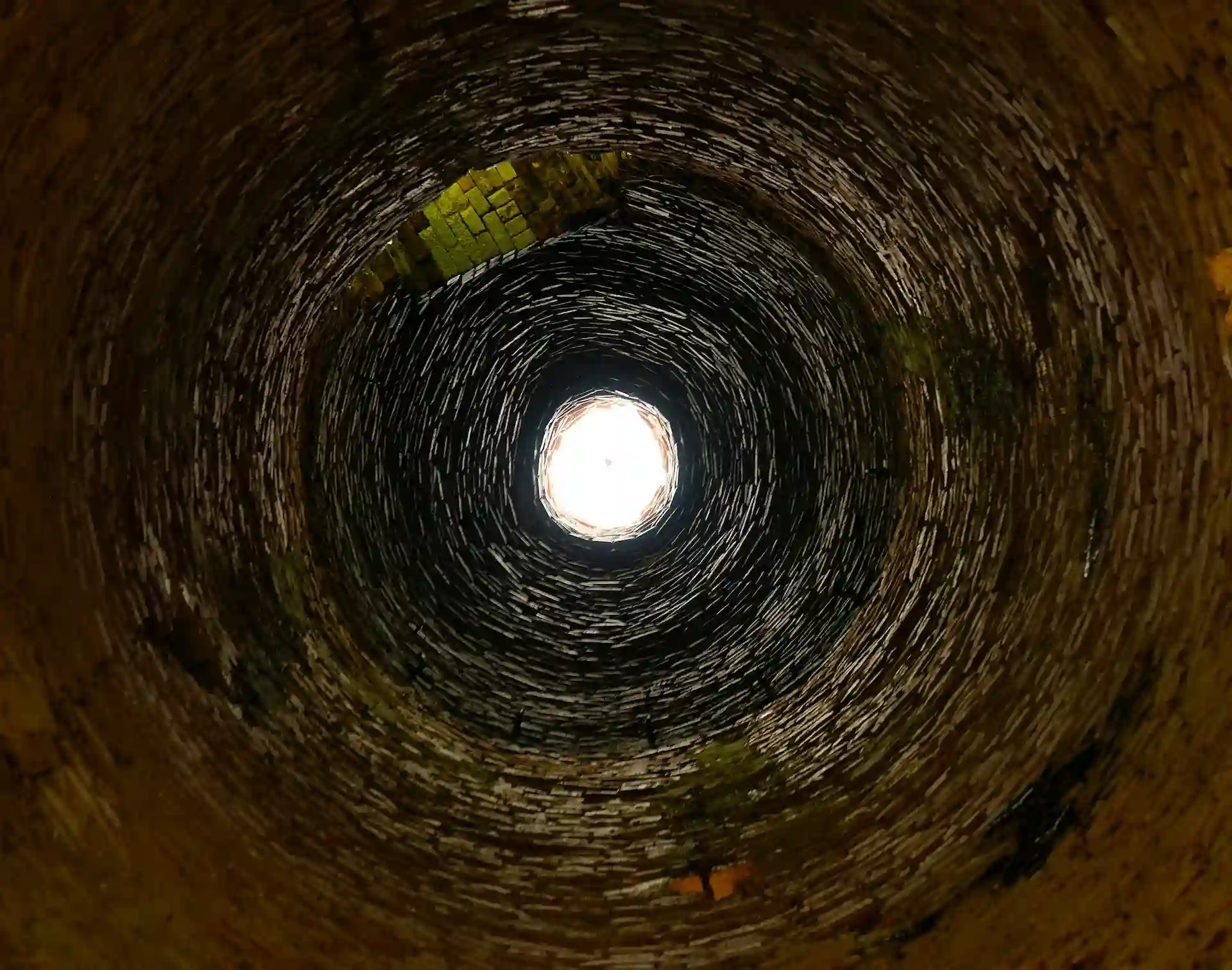 View from inside a stone well looking up towards bright circular light