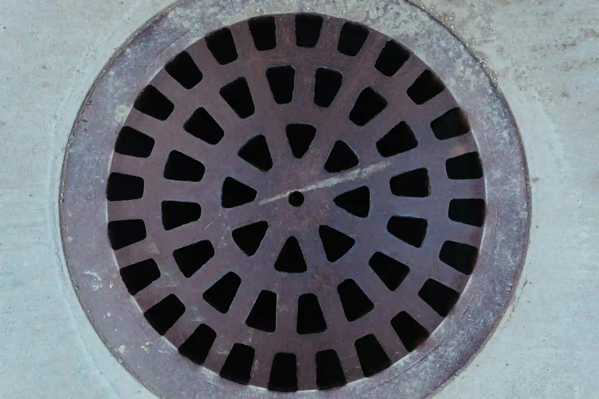 Round metal storm drain cover with radial black and gray pattern