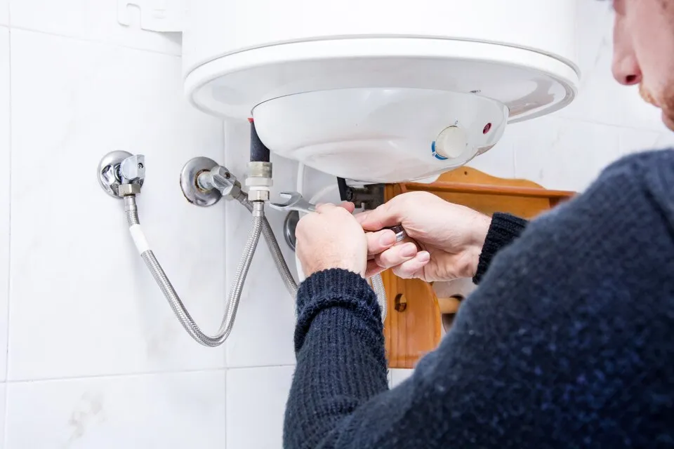 Technician repairing a white electric water heater with metal pipes
