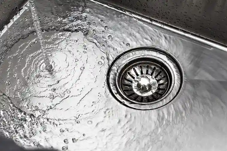 Water flowing into metal sink drain with rippling water surface