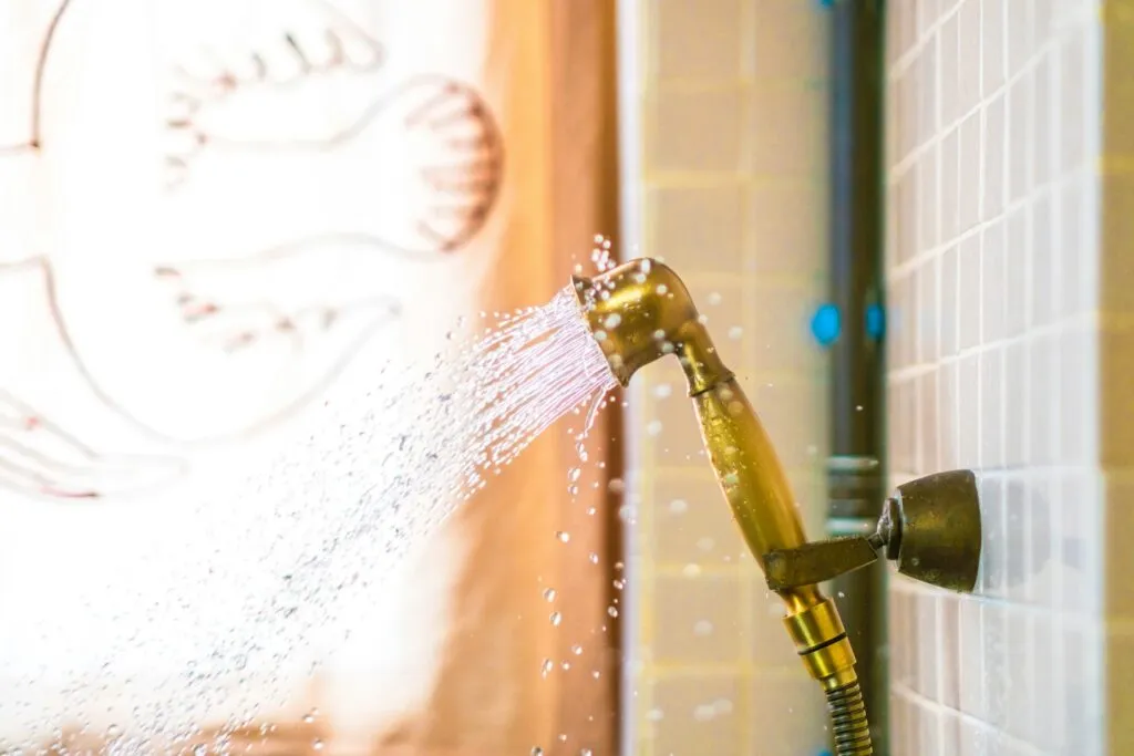 Water spraying from golden showerhead against tiled bathroom wall