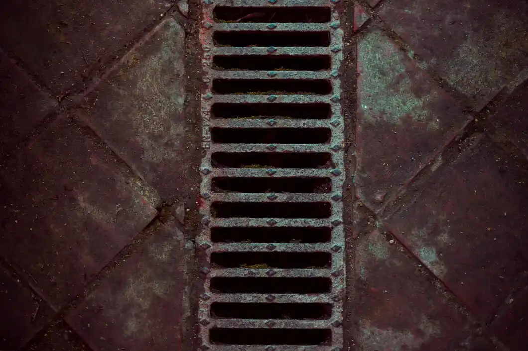 Rusty metal storm drain grate with patina on textured dark surface