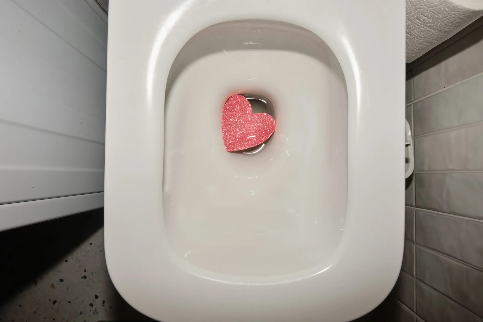 Pink glittery heart-shaped object sitting in white toilet bowl