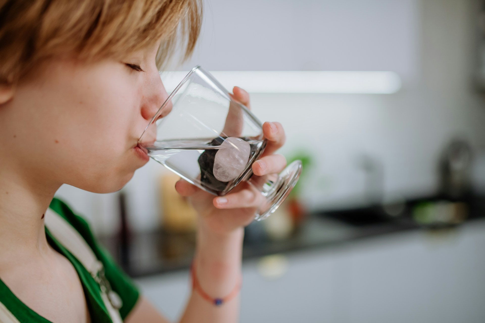 Young person drinking water from a clear glass with a stone inside