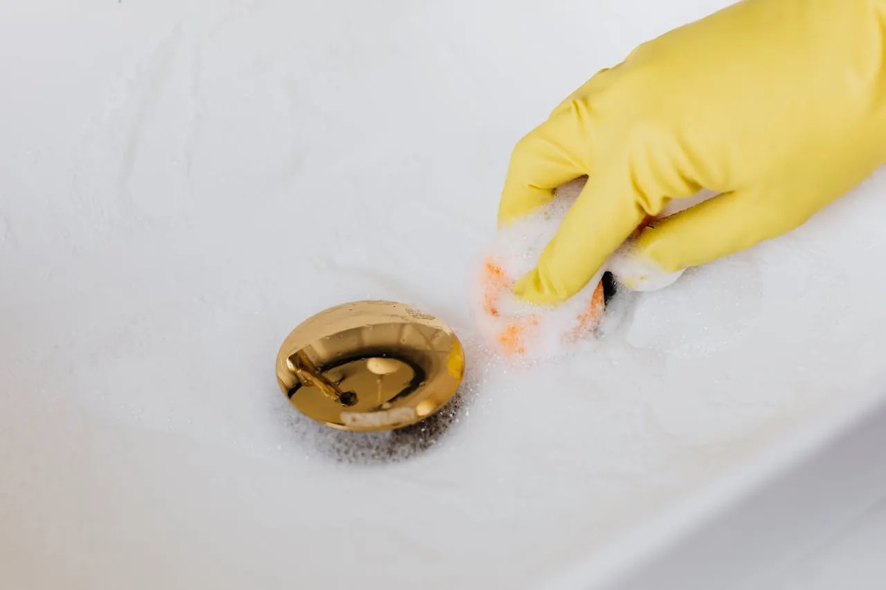 Yellow gloved hand cleaning drain with soapy sponge
