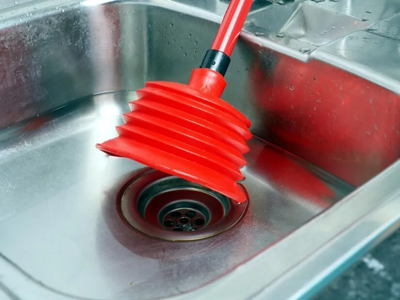 Red plunger on a stainless steel sink drain, ready to unclog