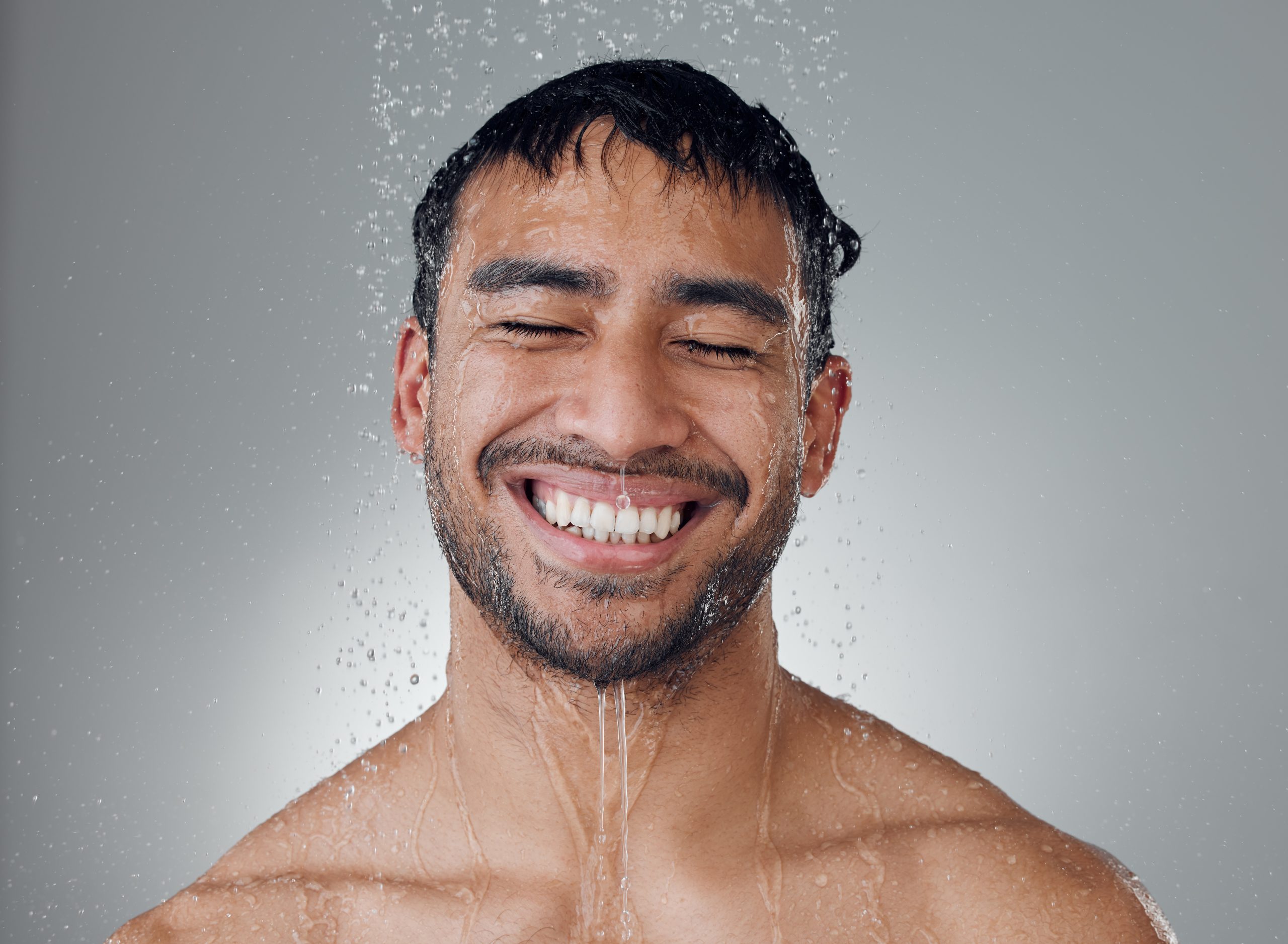 Person smiling with water droplets, eyes closed, enjoying shower