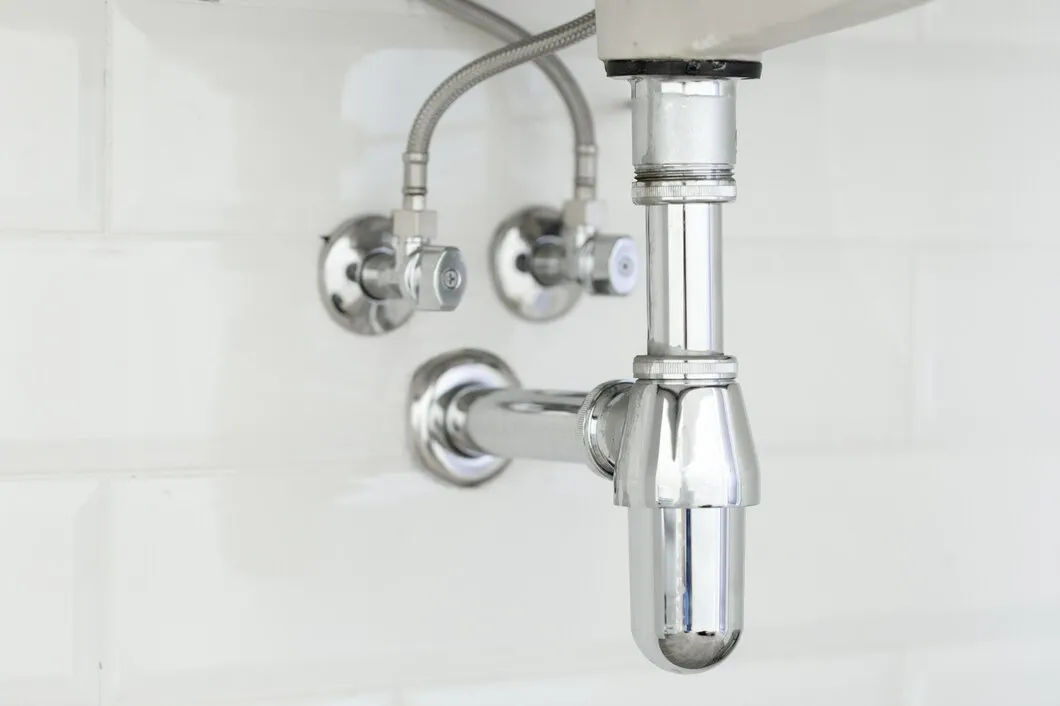 Chrome sink plumbing pipes and valves against white tiled wall