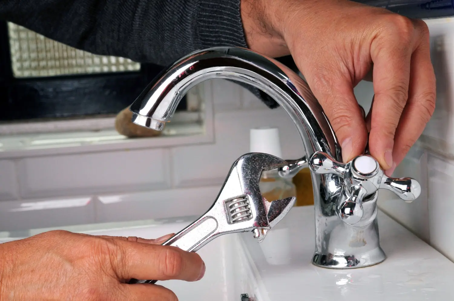 Hands using adjustable wrench to repair a chrome bathroom faucet