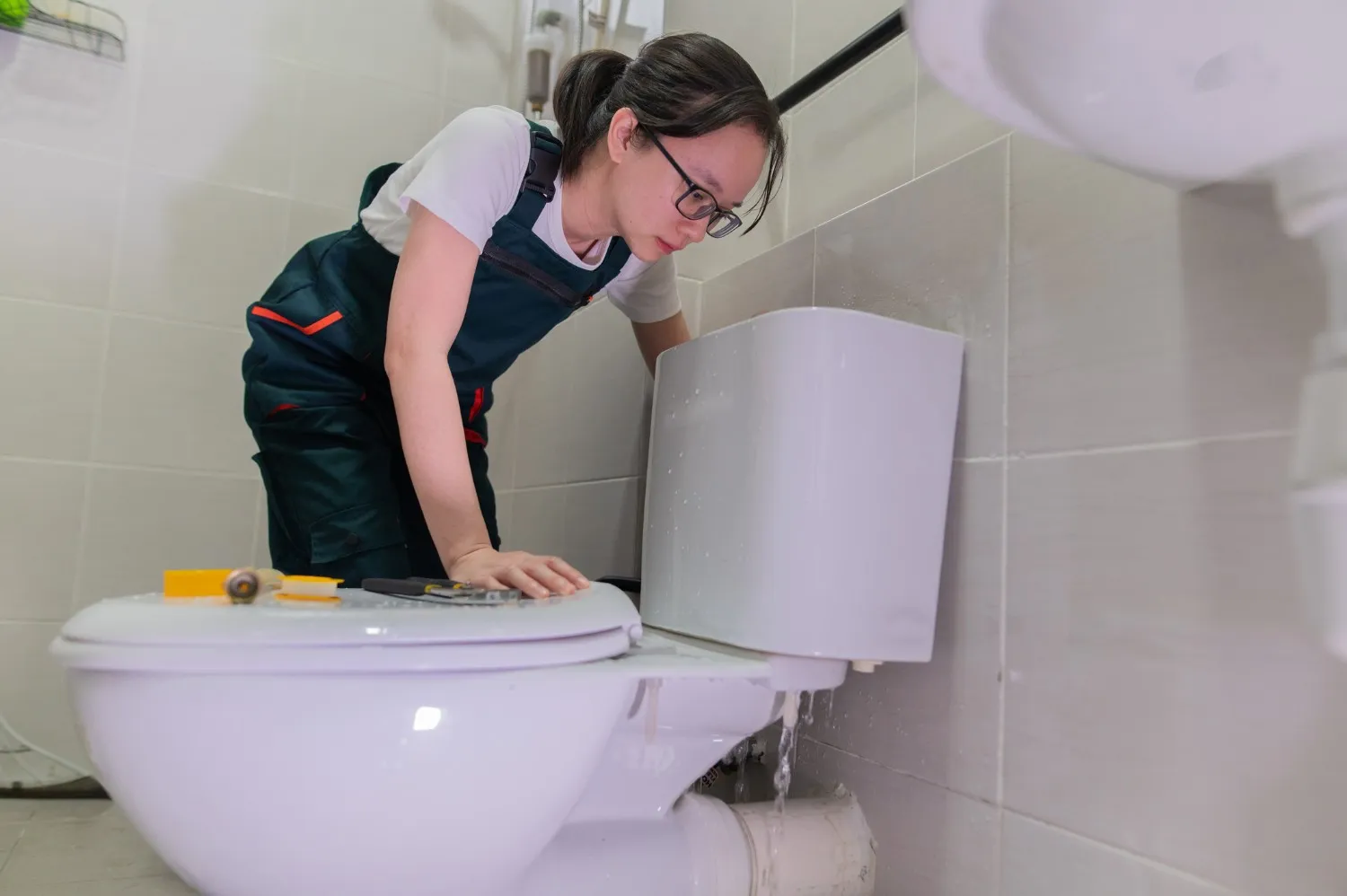 Plumber repairing toilet with tools in tiled bathroom