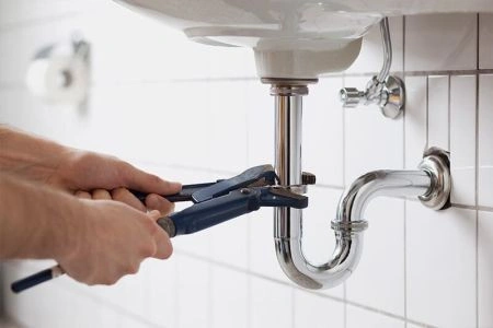 Plumber using wrench to fix bathroom sink pipe under white basin