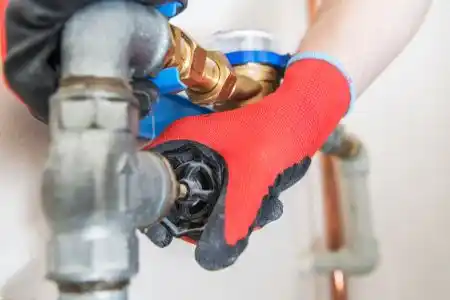 Plumber's hand in red glove fixing pipe connection with wrench