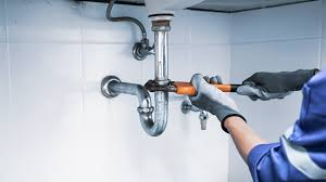 Plumber using wrench to repair sink pipes under bathroom sink