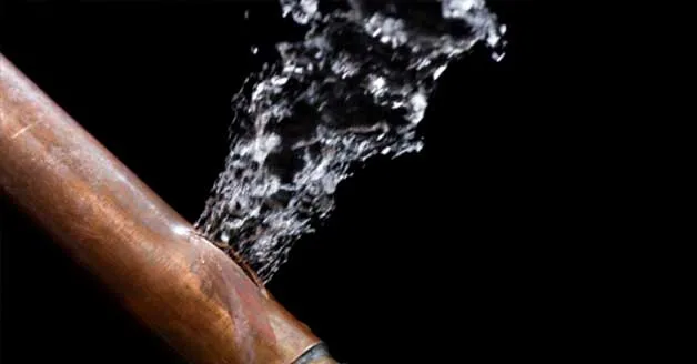 Water bursting from damaged copper pipe against dark background