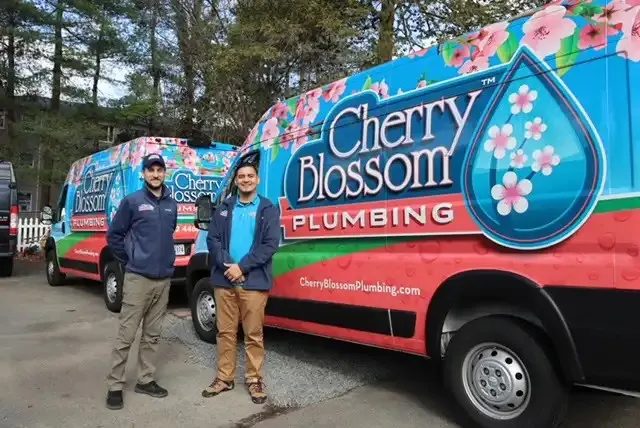 Two workers standing beside colorful Cherry Blossom Plumbing service van