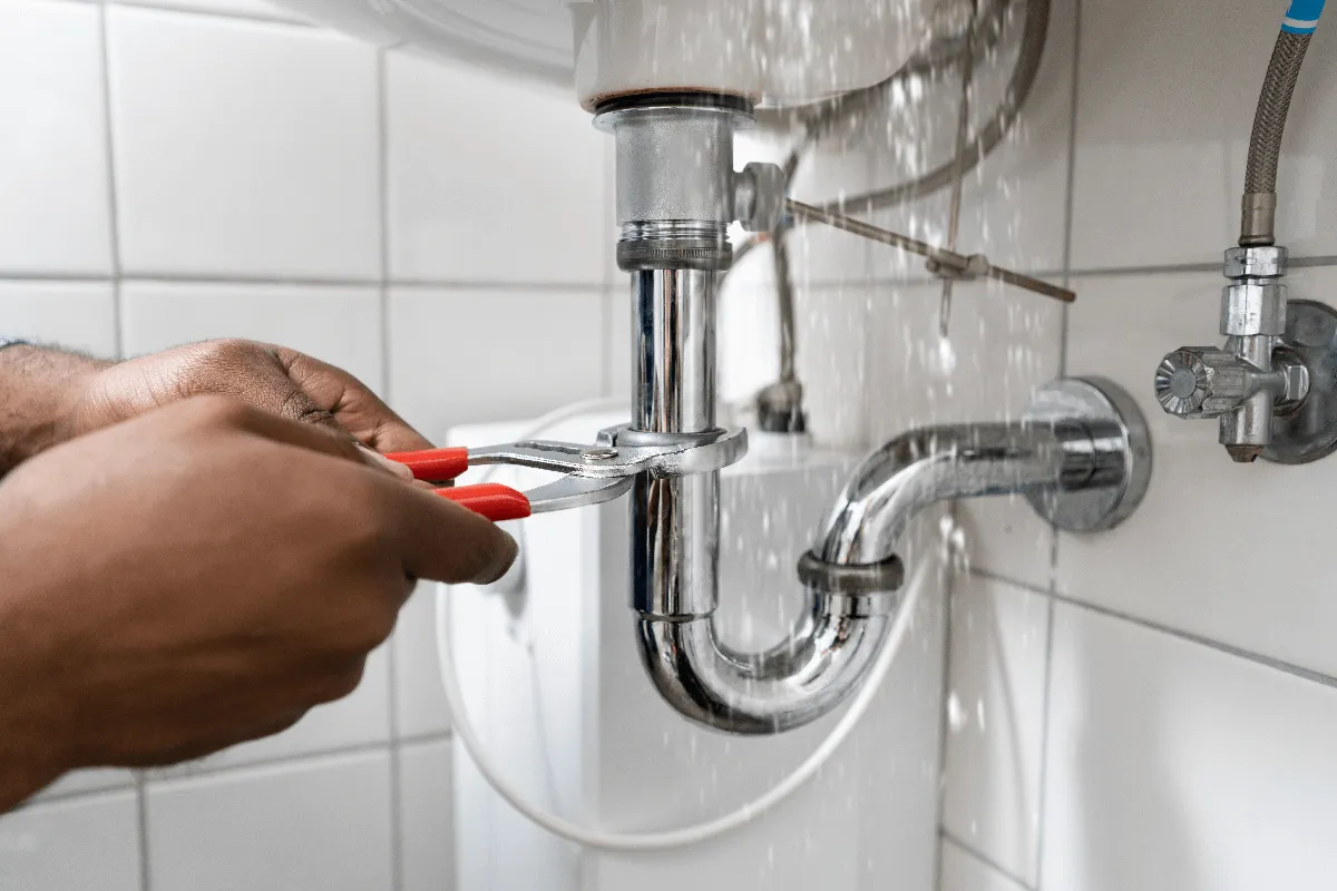 Plumber using wrench to repair sink pipes under bathroom sink