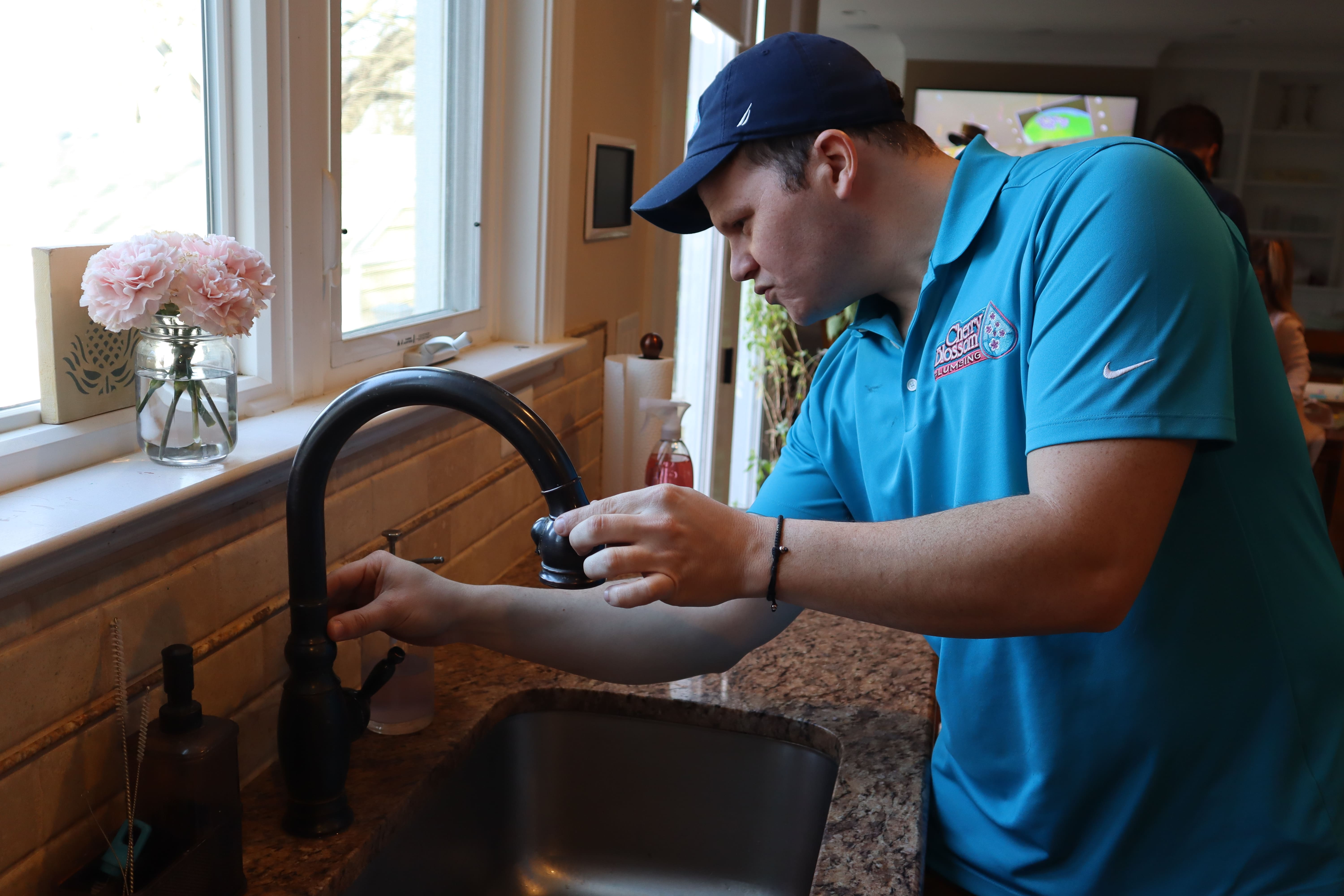 Plumber in blue shirt working on kitchen sink with pink flowers nearby