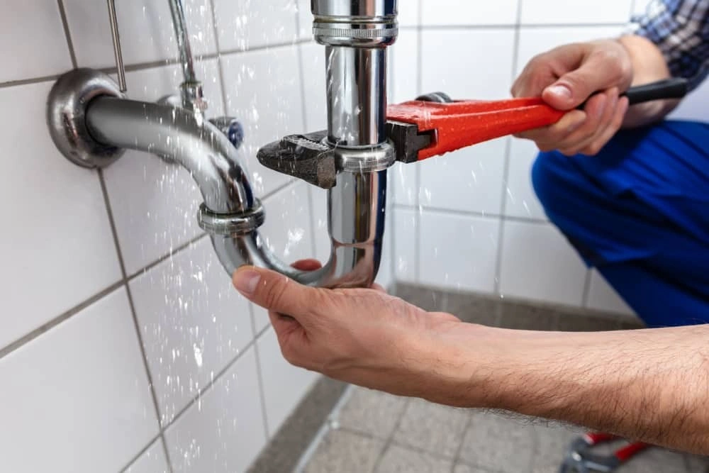 Plumber using red wrench to repair leaking sink pipe