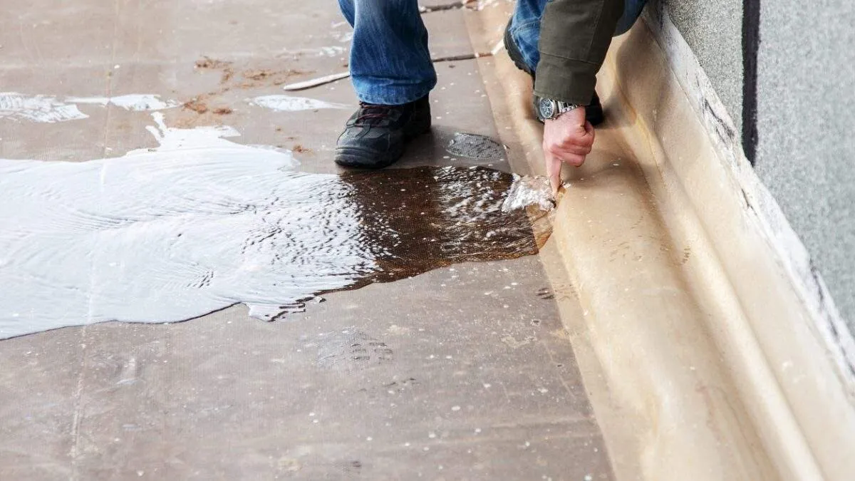 Person cleaning water puddle on floor with hand near concrete wall
